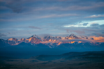 Wall Mural - scenic mountain landscape with great snowy mountain range lit by orange dawn sun among low clouds. a