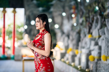 beautiful Asian young woman wearing red traditional Chinese cheongsam decoration Stand for pray to buddha statue for Chinese New Year Festival at Chinese shrine in Thailand