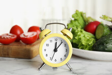 Alarm Clock And Vegetables On White Marble Table. Meal Timing Concept