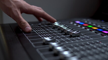 Man works on a professional electronic audio mixer. A control panel for tuning sound channels.