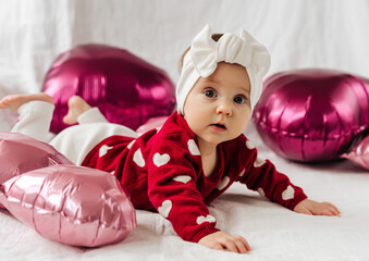 stylish infant in trendy white headband on bed with balloons. .cute baby girl in red sweater with he