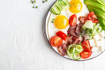 Healthy nutritious paleo keto breakfast. Fried eggs, bacon, avocado, cheese and fresh salad. on white plate. Flat lay