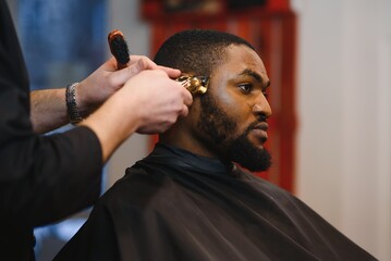 Closeup of process of trimming of hair in barber shop. Qualified barber keeping clipper in hands and correcting shape of hair to male client sitting on chair. Concept of haircut and shaving.