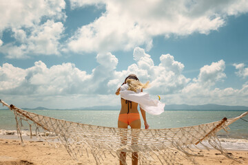 Wall Mural - Young woman in white shirt and hat standing with her back on tropical beach enjoying vacation