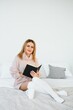 © Serhii - A woman reading a book and smiling as she sits in bed. The alarm clock on the desk beside her.
