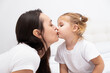© Юля Шевцова - adult brunet mother kissing her little blond daughter, white background.