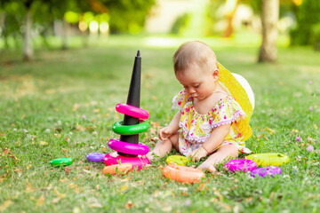 baby girl playing with a pyramid on the lawn in the summer, play in the fresh air, the concept of early development of children up to one year