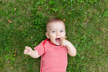 baby on the green grass in red clothes in the summer lies on his back, portrait