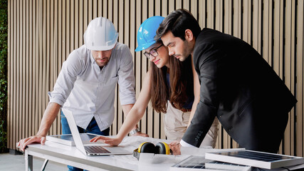 Three male architects in hardhats working together with laptop in concept of discussing project plan solar panels power and then celebrating success together. Concept of green electricity...