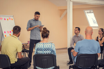 Group of people listening to a presentation. Man holding tablet and handling the workshop like a pro while speaking on seminar for professional development and team building