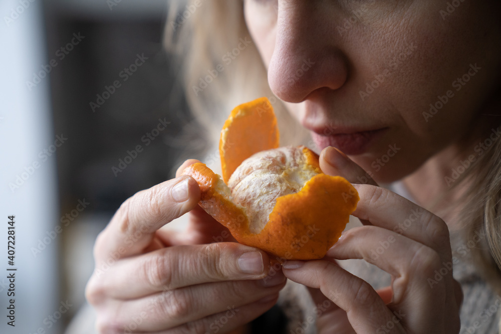 Sick woman trying to sense smell of fresh tangerine orange, has symptoms of Covid-19, corona virus infection - loss of smell and taste, standing at home. One of the main signs of the disease. - obrazy, fototapety, plakaty 