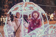 © EdNurg - Girl friends taking selfie photo in illuminated fairy tale carriage with horses decorated with lights and garlands for Christmas night and New Year holiday. Friendship and winter vacation concept