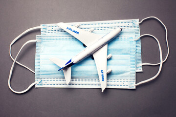 Wall Mural - Travel and health concept. Model of a white plastic airplane and masks on grey background.