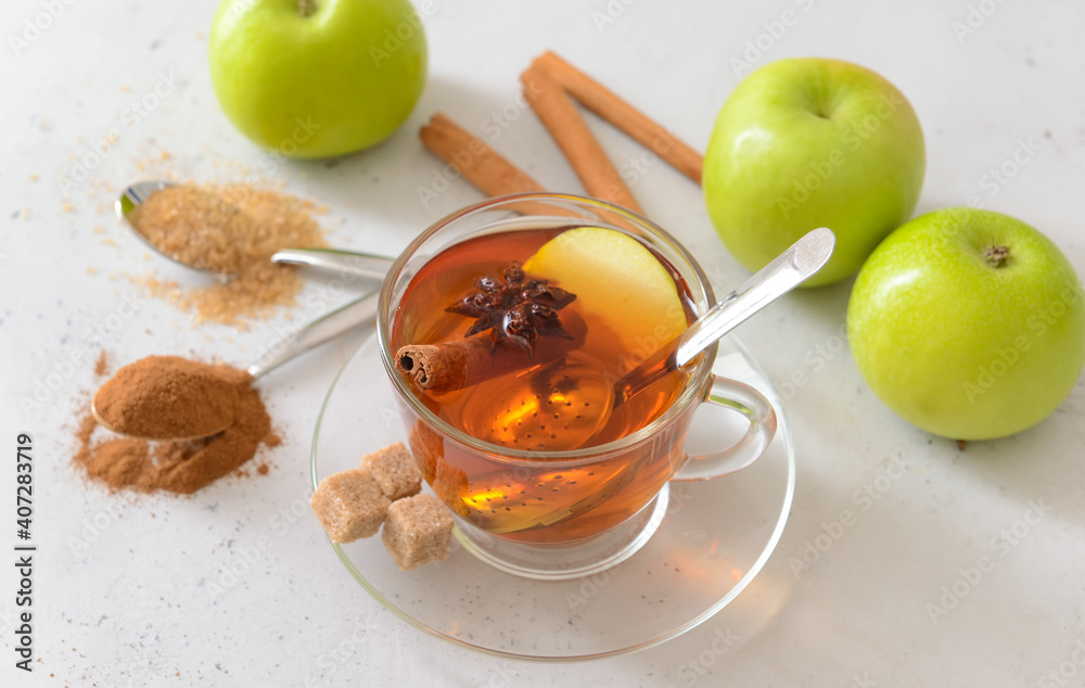 Tasty apple drink with cinnamon and anise in cup on light background