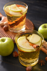 Tasty apple drink with cinnamon in glasses on dark wooden background