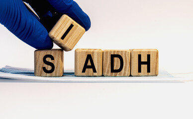 Text SIADH made from wooden cubes. Hands in a blue glove.