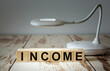 © Superzoom - A table lamp illuminates wooden blocks with the word INCOME
