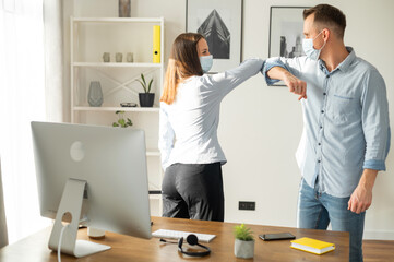 Poster - Greetings in the office during a pandemic, alternative handshake. Office employees in medical face masks greeting with elbow bump and smile to each other. Protective measures