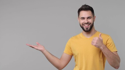 Wall Mural - Excited funny bearded young man 20s years old in yellow basic t-shirt isolated on grey color background studio. People lifestyle concept. Point index finger on empty palm showing thumb up like gesture