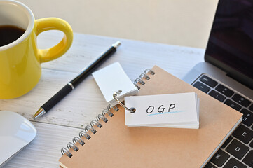 Poster - there's a word book on a desk with a cup of coffee and laptop pc. the word ogp is written in it. it'