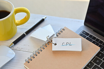 Poster - There's a word book on a desk with a cup of coffee and laptop pc. The word CPL is written in it. It's an abbreviation for Cost-per-Lead.
