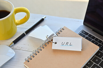 Poster - There's a word book on a desk with a cup of coffee and laptop pc. The word URL is written in it. It's an abbreviation for Uniform Resource Locator.