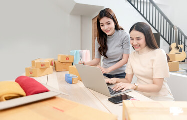 Two beautiful Asian women are checking orders by laptops via the internet. And pack the paper box With a happy smiling face, being a new normal online business