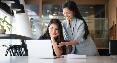 Two businesswoman using laptop computer and discussing business plan at modern startup office building.