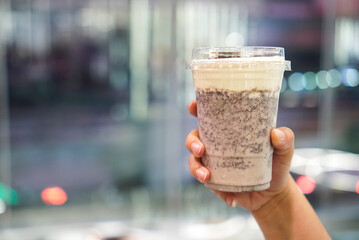 Wall Mural - Woman holding a plastic cup of cookies and cream smoothie (oreo mixed with milk) topped with cheese cream. Copy space.