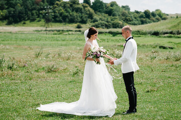 Wall Mural - Bride and groom walking and holding bouquet of flowers and greens, greenery on nature. Romantic couple newlyweds outdoors. Wedding ceremony.