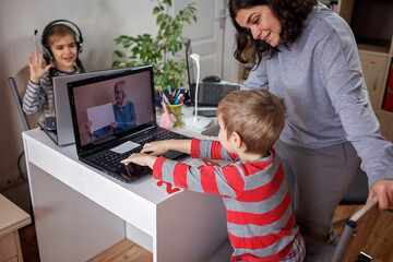 Distant education at home, children doing homework and mother working and help them. Elementary school kids during online class with parent working remotely in one room, self-isolation, quarantine