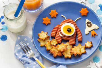 Wall Mural - Cute smiling alien shaped hamburger served with roast potatoes, carrots and eggs for a healthy lunch or dinner with yoghurt and orange juice. Fun food for kids