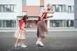 Side view of a joyful little girl playing hopscotch with her mother on playground outdoors. A child plays with her mom outside. A kid and mum play hopscotch drawn on the pavement outside.