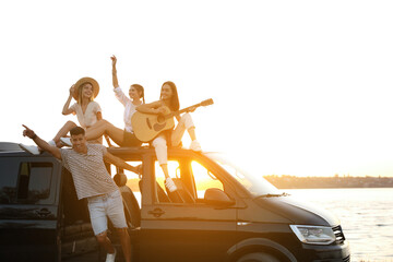 Wall Mural - Happy friends with guitar near sea at sunset. Summer trip