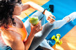 Sporty woman in sportswear training at home drinking fresh smoothie - Fit female athlete using smart watch to monitor her performance - Sport, food and technology concept