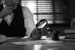 © New Africa - Old fashioned detective with magnifying glass working at table in office, closeup. Black and white effect