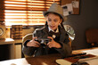 © New Africa - Cute little detective with camera at table in office