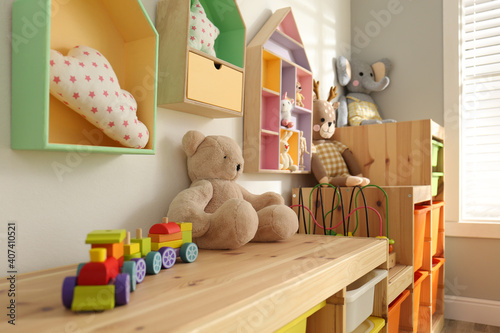 Colorful wooden toy locomotive and teddy bear on shelf in playroom. Interior design