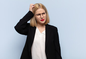 blonde woman feeling puzzled and confused, scratching head and looking to the side