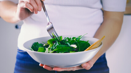 Wall Mural - Eating salad, woman standing eats a meal of salad. Fresh and light lunch. Organic vegetable, natural ingredients for healthy nutrition. Eating green food. Cooking vegetable