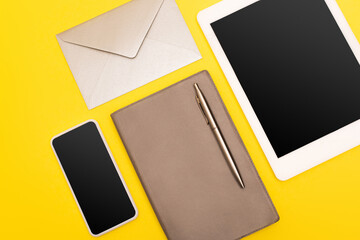 Canvas Print - top view of devices with blank screen near copy book with golden pen near envelope isolated on yellow