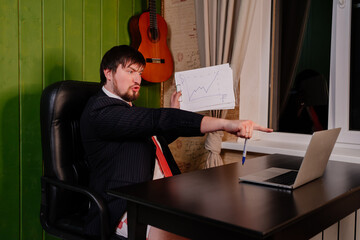 A man in shorts, a jacket and a tie draws a graph and leads a conference online