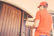 © Mangostar - Caucasian deliveryman going to wooden door and holding boxes. Middle-aged male courier delivering order at home and carrying parcels in cardboard package. Express delivery service and post concept