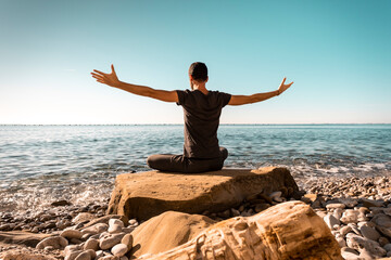 Attractive young man practicing yoga meditation and breathwork outdoors by the sea