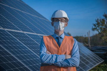 Wall Mural - Engineer, man in uniform and mask, helmet glasses and work jacket on a background of solar panels at solar station. Technician check the maintenance.