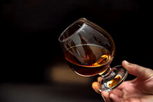 Glass Of Alcoholic Drink, Hold Cognac In Hands On A Dark Background