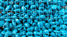Close Up To Blue Round Stones In The Grid. Large Stones Are Covered With Metal Wire Mesh Background. Natural Environmental Material Fencing. Blue Color Backdrop.