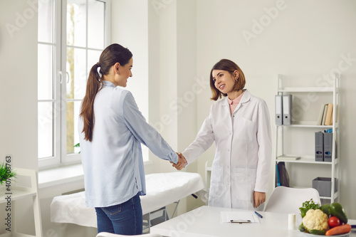 Female patient shakes hands with her dietitian thanking her for advice and consultation. Women in a modern medical clinic. Concept of a healthy lifestyle, doctor visits and professional advice.