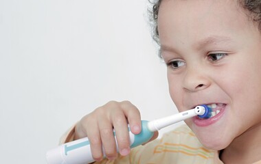 Wall Mural - boy brushing his teeth with an electric tooth brush on white background stock photo