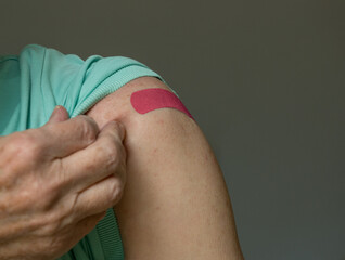 Senior caucasian man holding up shirt sleeve to show the bandaid after coronavirus vaccine shot in the shoulder